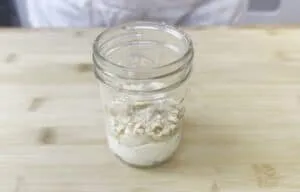Jar of layered flour and breadcrumbs on a wooden table.